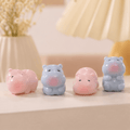 Four small hippo-shaped decorative figurines in pastel pink and light blue, arranged on a light surface with a softly blurred indoor background.