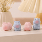Four small hippo-shaped decorative figurines in pastel pink and light blue, arranged on a light surface with a softly blurred indoor background.