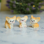 Three small pastel dog figurines with large ears and cute faces, arranged side by side on a light marble-like surface with a blurred purple floral background.